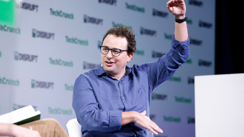 Dario Amodei, chemise bleue, une main levée, devant un fond TechCrunch Disrupt