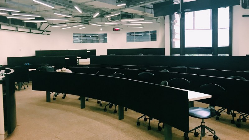 Salle de cours d’université vide : des gradins de tables noires et des sièges inoccupés, sous un éclairage blanc