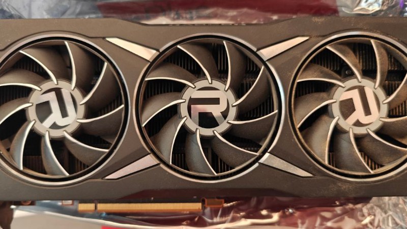 Carte graphique AMD Radeon RX 6800 XT photographiée de face : un carénage noir et argent et trois ventilateurs surmontés du logo Radeon.