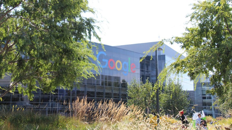 Façade vitrée du campus Google avec le logo coloré, derrière des arbres